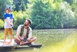 © moodboard - Smiling father looking at son standing on pier while fishing in lake