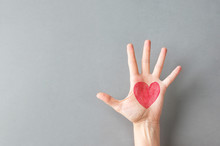 Hand Palm Of Young Caucasian Woman Girl With Painted On Red Heart On Gray Wall Background. Charity Love Donation Valentine Health Concept. Creative Social Poster Banner With Copy Space