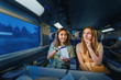 Two girl friends passengers sitting in first class train at night time, and eating chips