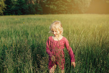 Cute Adorable Beautiful Preschool Caucasian Girl Walking In Tall High Grass On Meadow At Sunset. Happy Child Kid Enjoying Summer. Lifestyle Authentic Childhood. Village Rustic Rural Life.