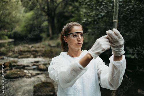 Fotografía Female scientist biologist and researcher in protective suit taking water samples from polluted river