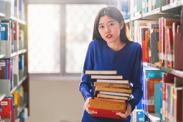 Wall Mural - Asian young Student in casual suit holding after searching the book from book shelf in library of university or colleage with various book background, Back to school concept