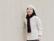 Beautiful Young Brunette Woman In White Beret And Woolen Sweater Smiling With Street Wall Background. Outdoor Fashion Portrait Of Glamour Young Chinese Cheerful Stylish Lady, Street Photography.