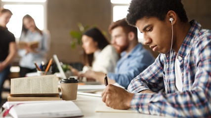 African-american guy preparing for exam, taking notes in library