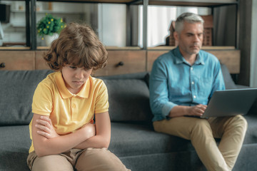 Wall Mural - Upset kid sitting near busy father on couch