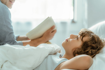 Wall Mural - Kid lying in bed while father reading book