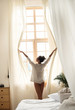 © Yakobchuk Olena - Attractive lady in shirt opening curtains in the morning
