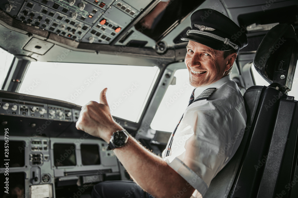 Smiling pilot in cockpit looking at camera - obrazy, fototapety, plakaty 