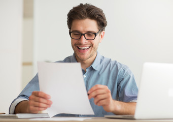 Poster - Cheerful Man Reading Financial Report At Laptop Indoor