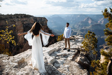 The Girl In A Chic Dress Spread Her Arms Like A Bird, The Guy Is Standing Opposite. Spectacular Canyon View In The Background