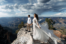 The Girl In A Chic Dress Spread Her Arms Like A Bird, The Guy Is Standing Opposite. Spectacular Canyon View In The Background