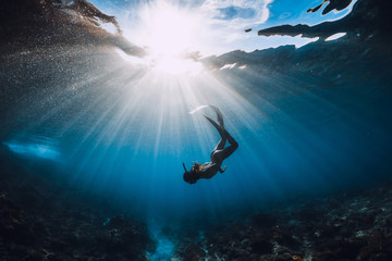 Wall Mural - Free diver woman with fins over coral bottom and amazing sun rays.