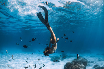 Wall Mural - Woman freediver with fins over sandy sea with fishes