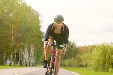 Sportswoman in uniform and helmet riding on the bike path on the background of green trees