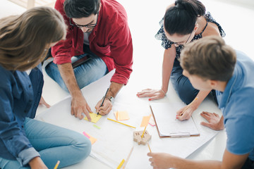 Group of young creative people are sitting on the ground floor to brainstorming, talking, planing. Team of creative co-workers using tool and papers to planning the work. Co working space concept.