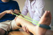 © wutzkoh - Patient use resistance band stretching out his leg with physical therapist helps in clinic room.