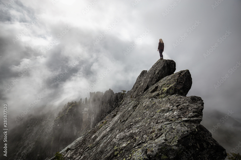 Adventurous Girl on top of a rugged rocky mountain during a cloudy summer morning. Taken on Crown Mountain, North Vancouver, BC, Canada. Concept: Explore, Adventure, Travel, Hike - obrazy, fototapety, plakaty 