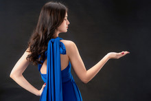 Beautiful Woman Fashion Model In Blue Dress Standing On Dark Background. Luxury Advertising.