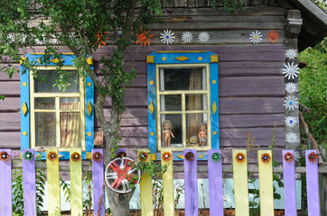 Two windows in the village house, shutters, platbands. The wall of the house is decorated with cut and painted plastic bottles