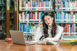 © THANANIT - Asian young Student in casual suit thinking when doing homework and using technology laptop in library of university or colleage with various book and stationary over the book shelf, Back to school