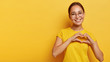 © wayhome.studio  - Lovely korean woman with happy smile, shapes heart with both hands, expresses love to you, wears round spectacles and yellow t shirt, says be my valentine flirts with boyfriend poses indoor copy space