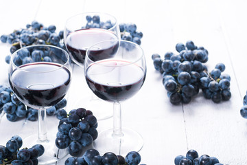 Canvas Print - three glasses of red wine and blue grapes on white wooden table background