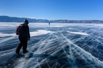 Frozen Lake Baikal. Two people silhouettes walk on the ice surface on a frosty day with beautiful mountain. Natural background