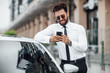 © Тарас Нагирняк - Handsome, smiling, happy, bearded businessman is using smartphone and standing near his car outdoors on the streets.