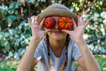 Cute little girl holding a bunch of fresh organic tomatoes in her eyes.