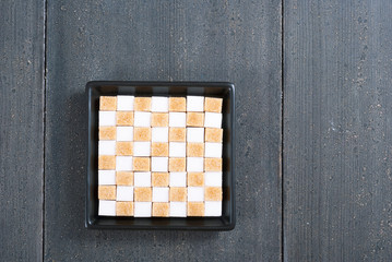 Canvas Print - brown and white sugar nubs on black square plate, wood table