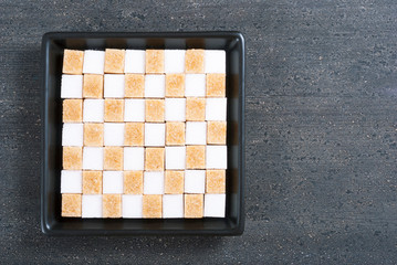 Canvas Print - brown and white sugar nubs on black square plate, wood table