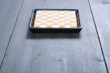 brown and white sugar nubs on black square plate, wood table