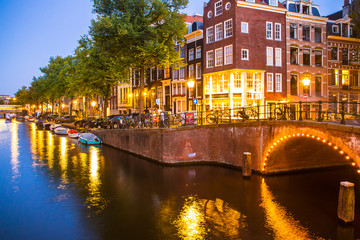 Fototapete - Amsterdam seen in the evening with light, canal and bridge