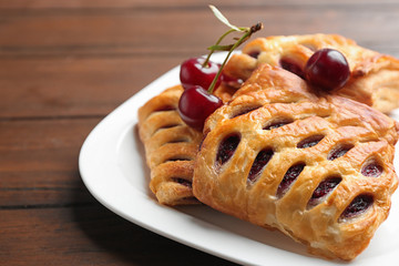 Fresh delicious puff pastry with sweet cherries served on wooden table, closeup