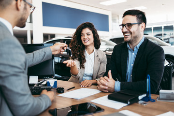 Middle age couple choosing and buying car at car showroom. Car salesman gives them car keys.