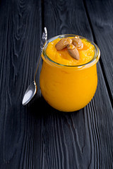 Wall Mural - Puree with pumpkin, almonds  and honey in the glass jar on the black wooden background. Copy space. Location vertical.