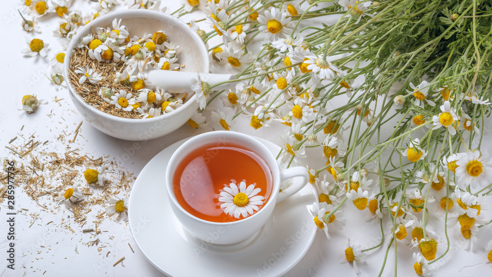 Rural still-life - cup of brewed chamomile tea on the background of a bouquet of daisies, closeup - obrazy, fototapety, plakaty 