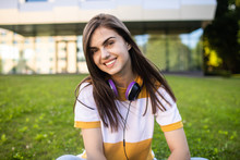 Portrait Of Smiling Cute College Girl With Headphones Posing In Front Of Her Alma Mater
