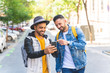 © MCStock - Two Male Friends Walking Together in the Street While Using Cell Phone.