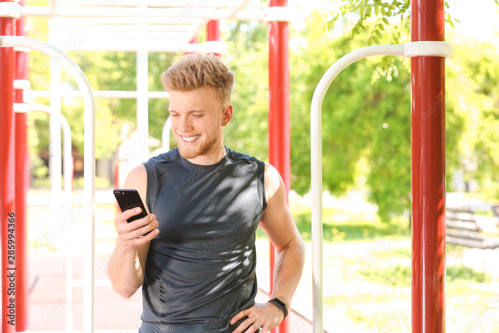 Sporty young man with mobile phone outdoors