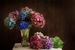 © Karynf - Beautiful hydrangea flowers in multiple colors arranged in a vase on a table; Bright pink, purple and blue bunches of flowers