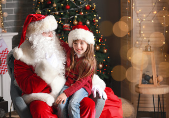 Santa Claus and little girl in room decorated for Christmas