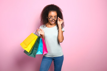 Portrait of beautiful African-American woman with shopping bags on color background