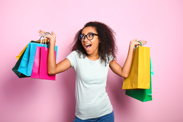 Portrait of happy African-American woman with shopping bags on color background