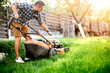 © aboutmomentsimages - Gardening details, garden worker starting the lawnmower and cutting grass in garden.