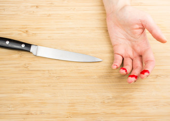 Child playing with knife. One hand with wounded bleeding fingers and kitchen knife on a wooden cutting board