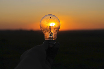 man's hand holding a bulb against rising sun