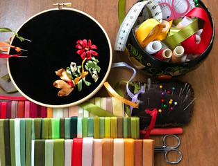 The process of embroidery with satin ribbons a floral ornament in red, golden and green color on black velvet (embroidery made author of photo). Accessories for embroidery, needles and sets of ribbons