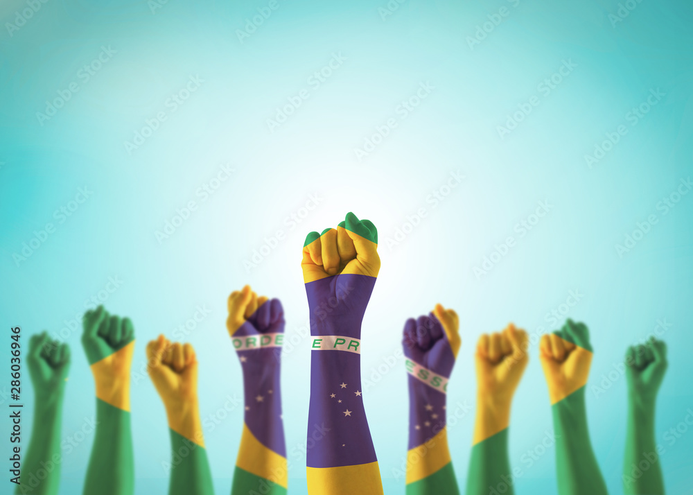 Brazil flag on people hands with clenched fists raising up for labor day national holiday celebration and stay strong for Brazilian power isolated on blue sky background (clipping path) - obrazy, fototapety, plakaty 