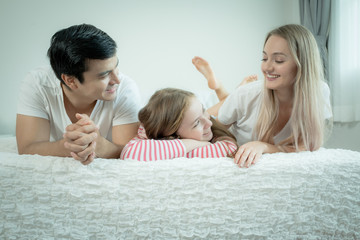 little girl smiling with mother and father on bed together in bedroom at home, young happy family concept